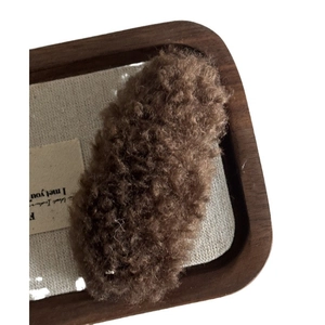 Brown teddy plush hair clip on a minimalist linen background with wooden frame decor