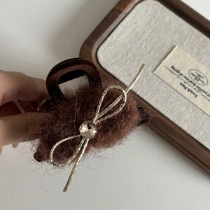 Détail de la pince à cheveux en peluche marron avec un nœud doré et un strass brillant