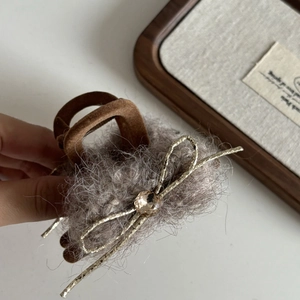 Détail d'une pince à cheveux grise en peluche avec nœud doré et pierre de cristal