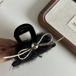 Vue détaillée de la pince à cheveux en peluche noire avec nœud doré et cristal