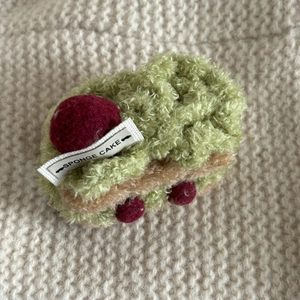 Close-up of green plush sponge cake hair clip with strawberry detail on knit background