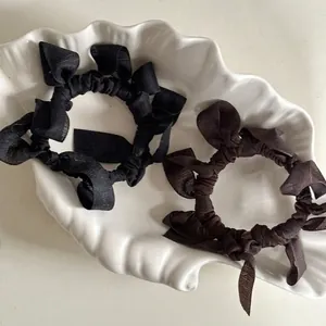 Elegant bow hair ties in black and dark brown silk fabric on a white ceramic plate