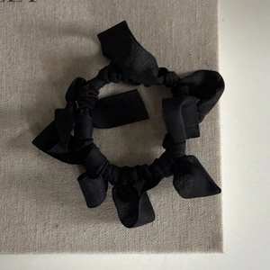 Elegant black layered bow hair scrunchie with soft fabric texture on linen background