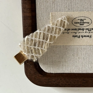 Detailed close-up of French wool knit hair clip with gold metal base on wooden tray