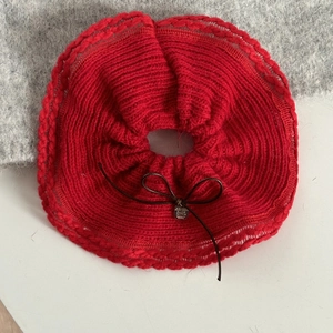 Détail d'un chouchou en tricot rouge avec un nœud marron et un petit pendentif argent