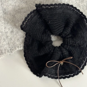 Détail d'un chouchou en tricot noir avec bords au crochet et noeud décoratif marron