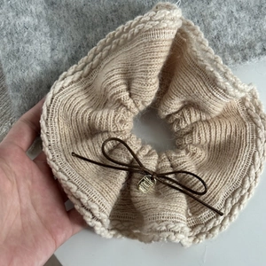 Détail d'un chouchou en tricot beige avec un petit pendentif métallique doré ovale
