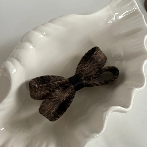 Close-up of a vintage brown tweed bow hair clip placed on a white shell-shaped tray