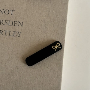 Détail d'une barrette à cheveux en velours noir avec un nœud doré posée sur un livre