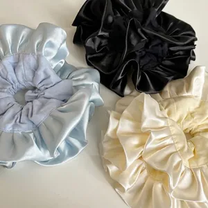 Three oversized satin ruffle scrunchies in black, light blue, and creamy white colors