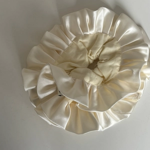 Detail of cream pleated satin hair scrunchie with elegant ruffled texture and glossy finish