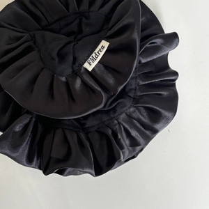 Detailed macro view of black satin hair bonnet with pleated ruffle edges and brand label