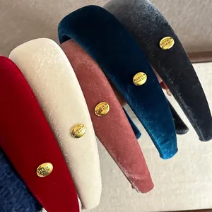Wide velvet headbands in multiple colors with gold emblem detail for women
