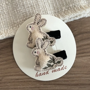 Close-up of handmade cream rabbit hair clips with green floral embroidery and dark stitching