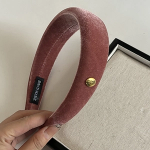 Close-up of velvet wide headband in dusty rose pink with golden metal logo detail