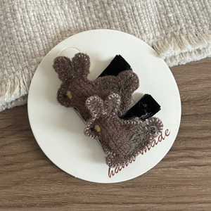 Detail of two handmade brown embroidered bunny hair clips on a white display card
