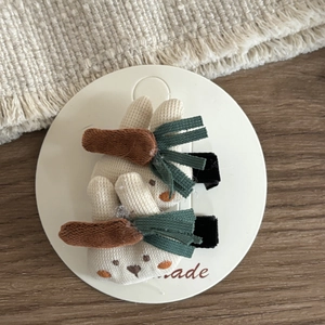 Detail of two handmade knitted rabbit hair clips with carrot accents on a card