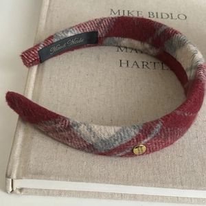 Red and white plaid tweed headband with gold emblem on a fabric book background