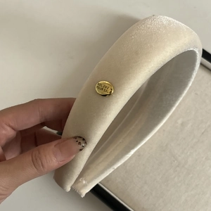 Detail of beige velvet headband featuring a gold metal tag with Believe engraving