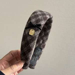 Handheld view of wide plaid headband featuring a black velvet bow and golden metal charm