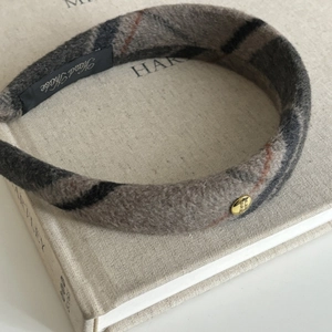 Close-up of wide wool plaid headband with golden metal tag and handmade label on a book