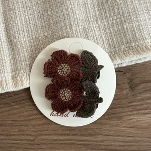 Detail of handmade crochet flower hair clips with dark brown petals and green leaves