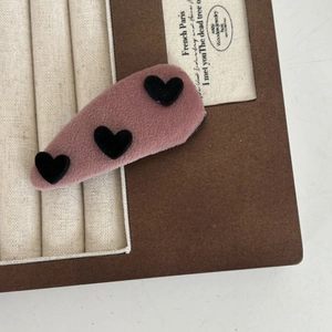 Détail d'une pince à cheveux en velours rose avec motifs cœurs noirs sur fond de bijoux