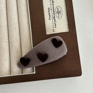 Gros plan d'une pince à cheveux en peluche grise avec trois motifs cœurs en velours