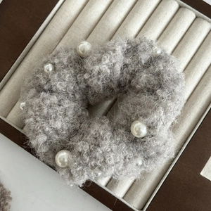 Nahaufnahme von grauem Plüsch-Scrunchie mit weißen Perlen auf einem Schmucktablett