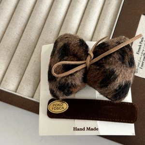 Detail of leopard print plush bow hair clip with velvet base and gold metal tag