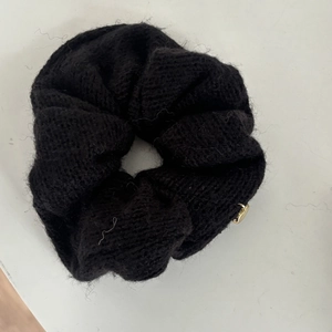 Detail eines schwarzen Strick-Scrunchies mit weicher Textur und goldenem Herzanhänger