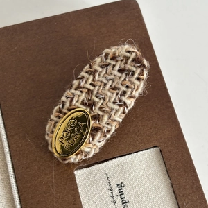 Close-up of brown tweed fabric hair clip with a gold metallic logo plate detail