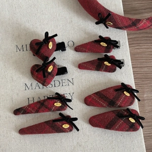 Close-up of red plaid fabric hair clips with black ribbon bows and gold metal accents