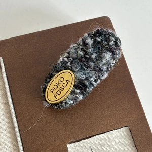 Detail of tweed fabric hair clip with a golden metal logo plate for hair styling
