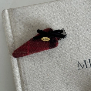 Detail view of red tweed hair clip featuring black velvet bow and golden Love emblem