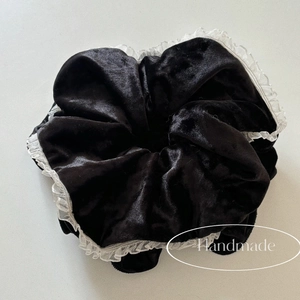 Close-up of black velvet scrunchie with white lace trim and handmade label detail