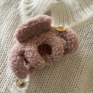 Fuzzy pink lamb wool hair claw clip with golden metal egg label on white knit background