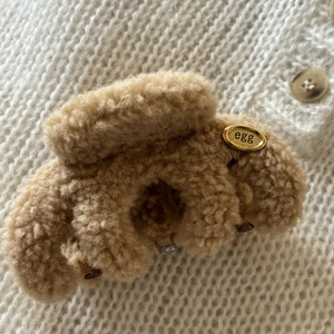 Macro shot of plush brown faux fur hair claw clip with golden egg label on knit background