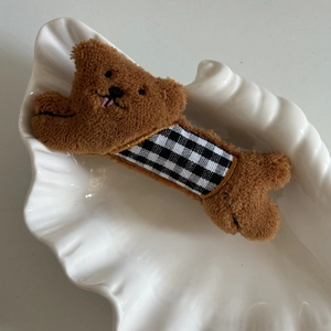 Barrette à cheveux chien en peluche marron avec nœud à carreaux sur plat blanc
