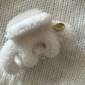 Macro detail of plush beige faux fur hair claw with a gold oval metal tag and egg engraving