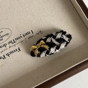 Detail of tweed hair clip with gold bow accent on a vintage fabric background