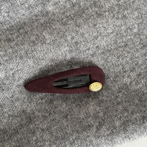 French vintage burgundy fabric BB hair clip with gold logo on grey knit background