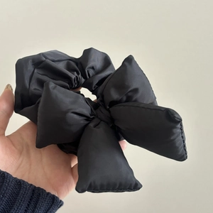 Detail view of a black padded bow hair tie showing the glossy fabric and puffy 3D texture