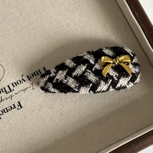 Close-up of houndstooth tweed hair clip featuring a delicate gold metal bow accent