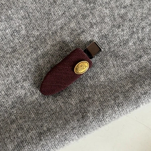 Close-up of wine red quilted fabric hair clip with a golden metal logo on knit background