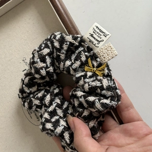 Close-up of black and white houndstooth tweed scrunchie with gold bow charm and label