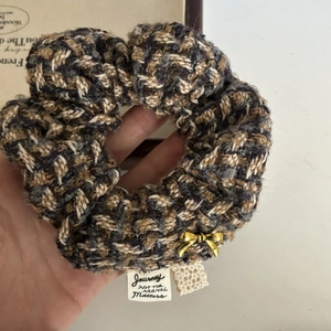 Detail of tweed hair scrunchie with gold bow charm and journey text woven label