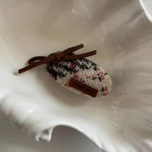 Detail of tweed hair clip with brown suede bow and sweet love leather label in a shell tray