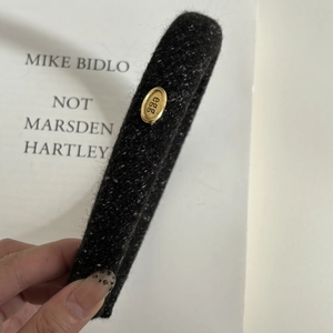 Detailed view of dark grey wool-textured headband with an oval gold egg metal tag
