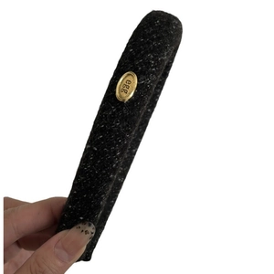 Handheld view of a premium black tweed headband featuring a gold oval metal egg emblem